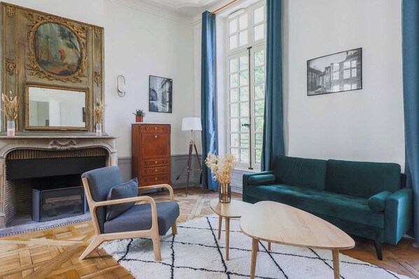 A living room with a fireplace, a green sofa, a blue armchair, and a coffee table. - Exceptional apt - 2br/4p- Notre-dame Cathedral (Paris)