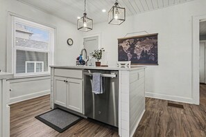 A modern kitchen with white cabinetry, a stainless steel dishwasher, and a world map on the wall.
