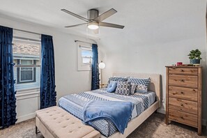 A bedroom with a bed, a dresser, a ceiling fan, and a window with curtains.