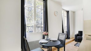 Un'elegante sala da pranzo moderna con un tavolo rotondo apparecchiato per due persone, un vaso di fiori e vista sulla città attraverso ampie finestre.