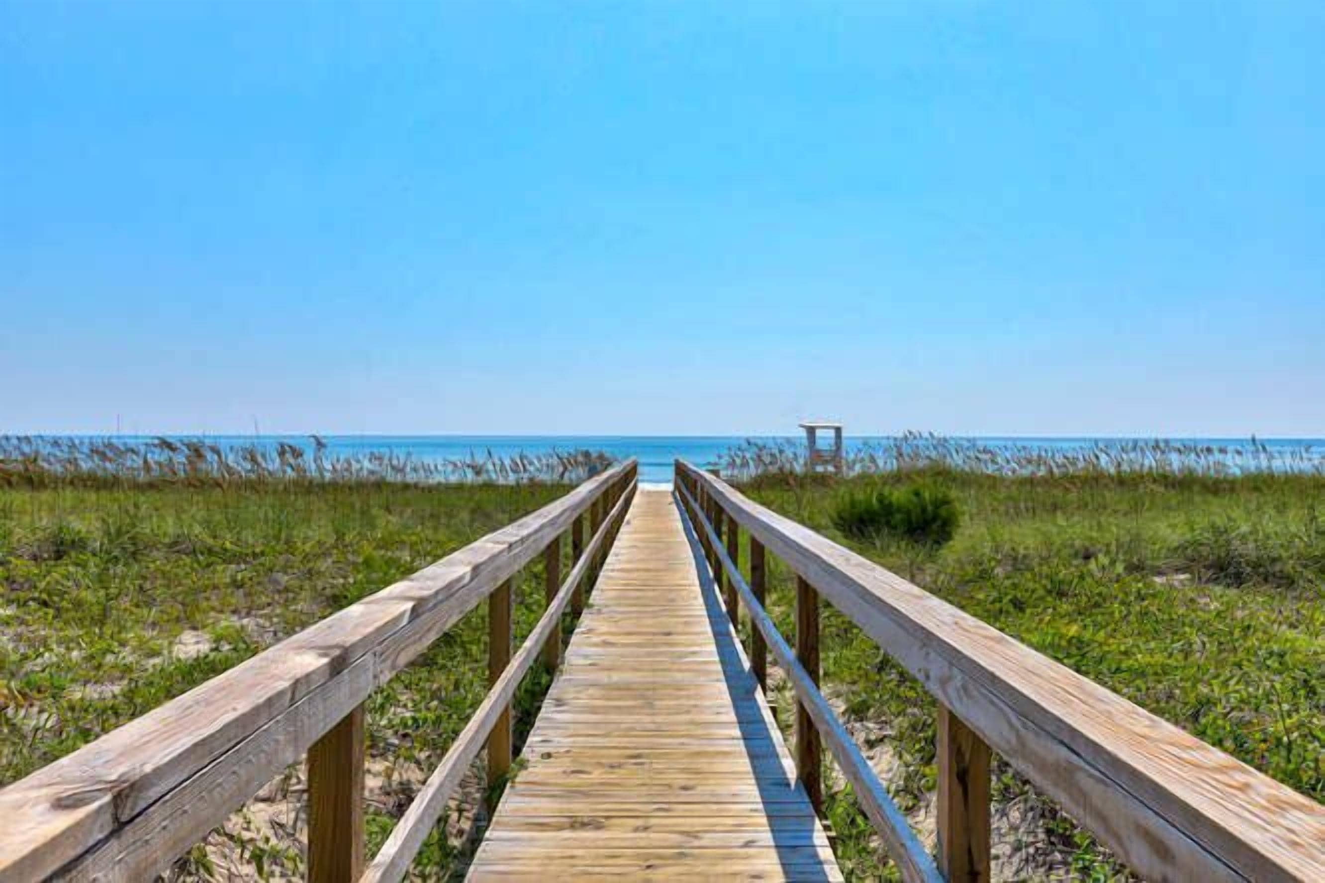 A wooden boardwalk leading to a beach with a clear sky.
