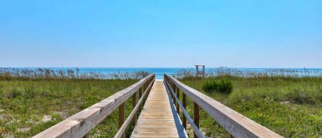 A wooden boardwalk leading to a beach with a clear sky.
