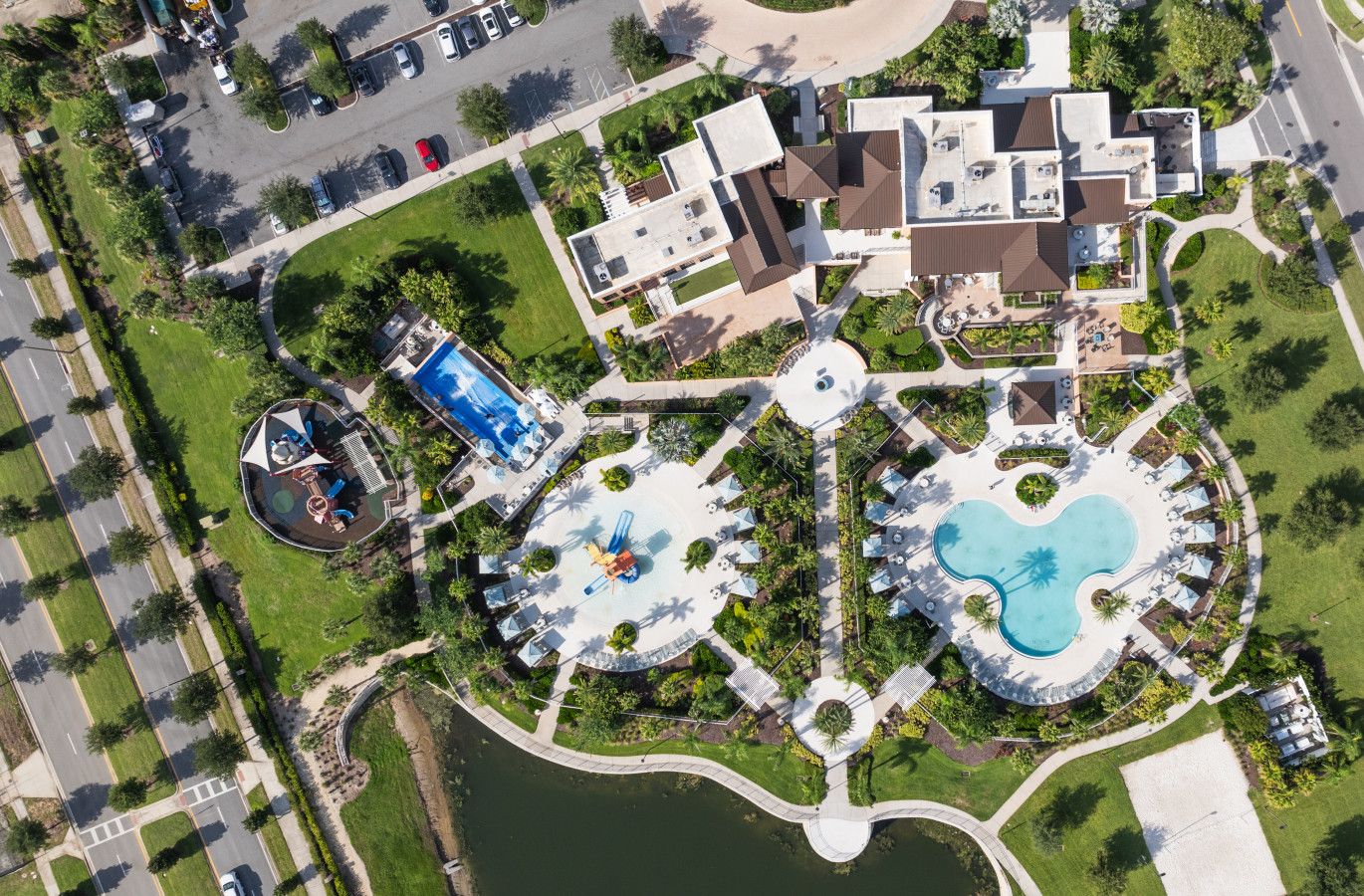An aerial view of a resort with multiple swimming pools, a children's play area, and a bridge over a body of water.