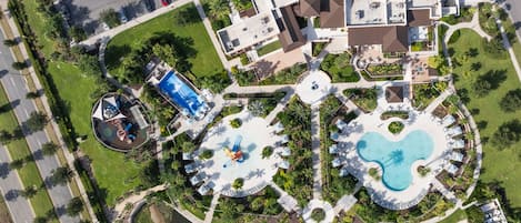 Vista aérea de un complejo turístico con múltiples piscinas, una zona de juegos infantiles y un puente sobre una masa de agua.