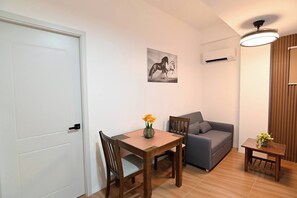 A small, well-lit room with a dining table, chairs, a sofa, and a small table with flowers.