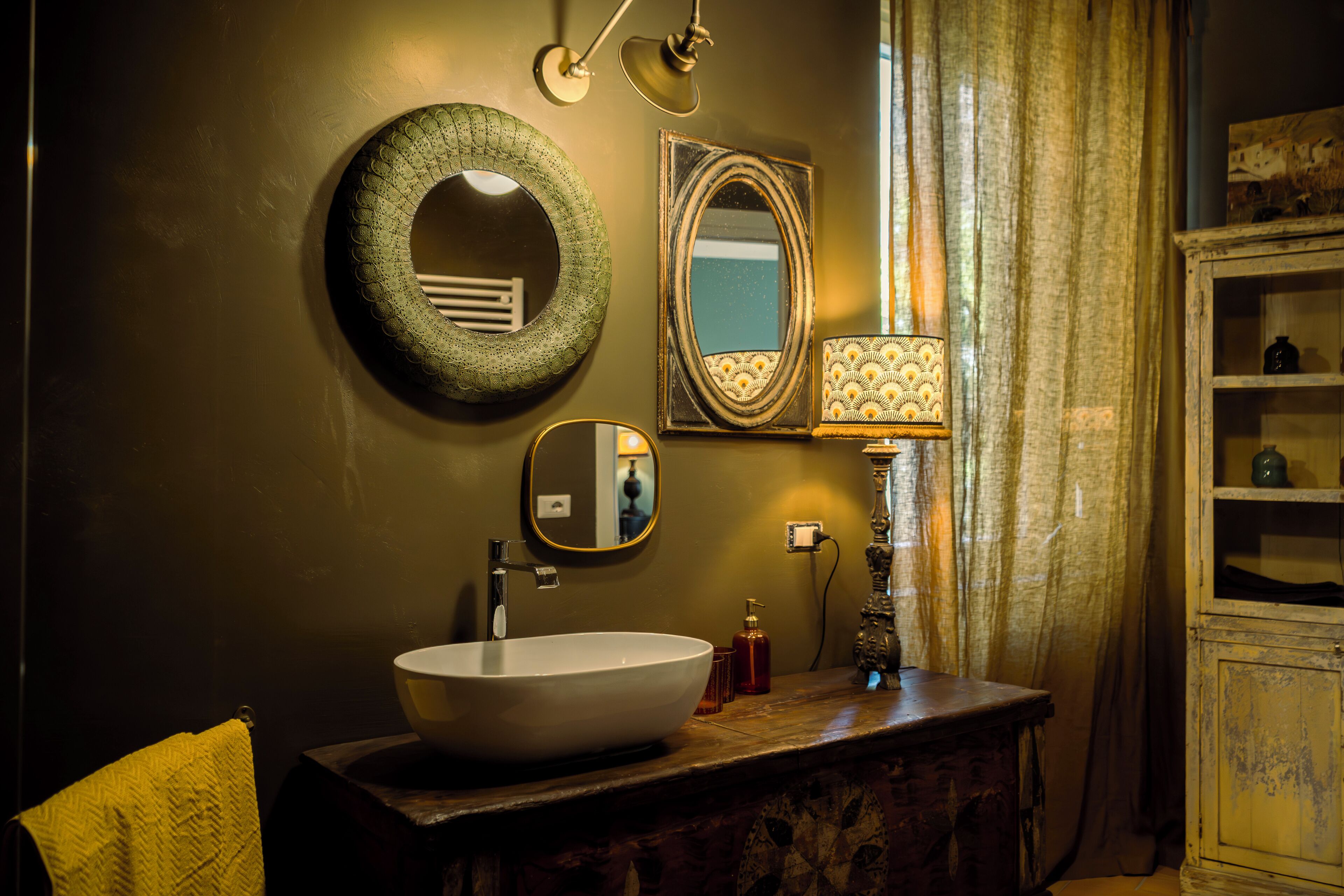 A bathroom with a round mirror, a rectangular mirror, a white sink, and a decorative lamp.