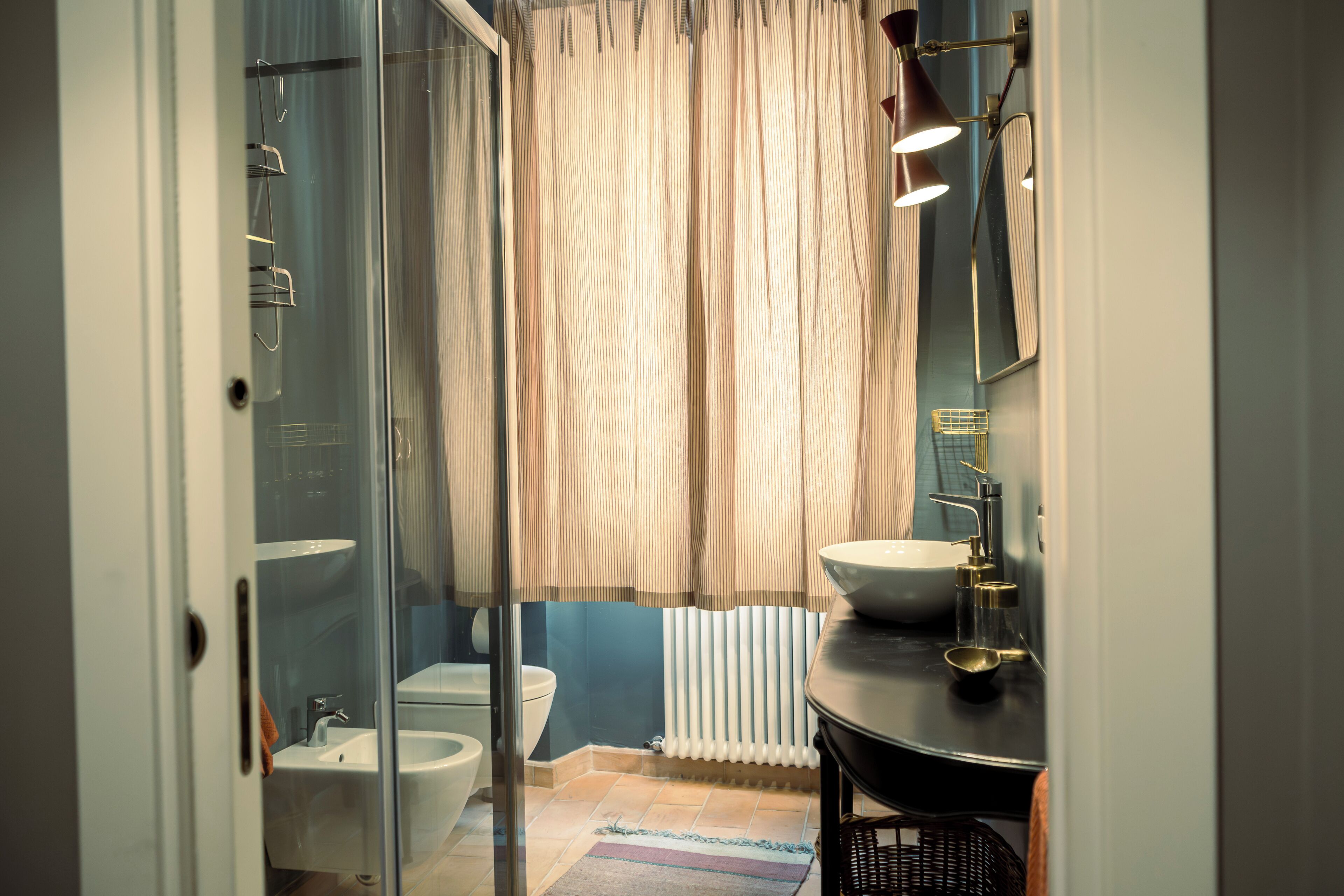 Un baño con cabina de ducha de vidrio, un lavabo blanco, un bidé y un radiador.