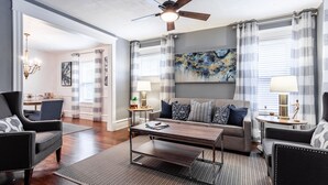 A modern living room with a sofa, two armchairs, a coffee table, and a ceiling fan. There is a dining area with a table and chairs in the background. - Beautiful Duplex In Kansas City! 13&14 v2 (Kansas City)
