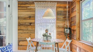 A wooden cabin interior with a round table, white chairs, a hanging light fixture, and a window with a view of trees. - Beautiful Duplex In Kansas City! 13&14 v2 (Kansas City)