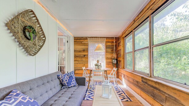 A cozy cabin interior with a sofa, a table, and chairs, large windows, and wooden walls. - Beautiful Duplex In Kansas City! 13&14 v2 (Kansas City)