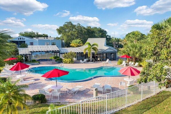A pool area with lounge chairs and umbrellas, surrounded by a fence and greenery. - Luxury House - Sleeps 8, Golf, Disney, Family Fun! (Orlando)