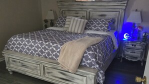 Un dormitorio con una cama grande, una mesita de noche con lámpara y una ventana con cortinas.