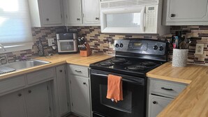 Una cocina con gabinetes grises, estufa negra, microondas y salpicadero de azulejos.