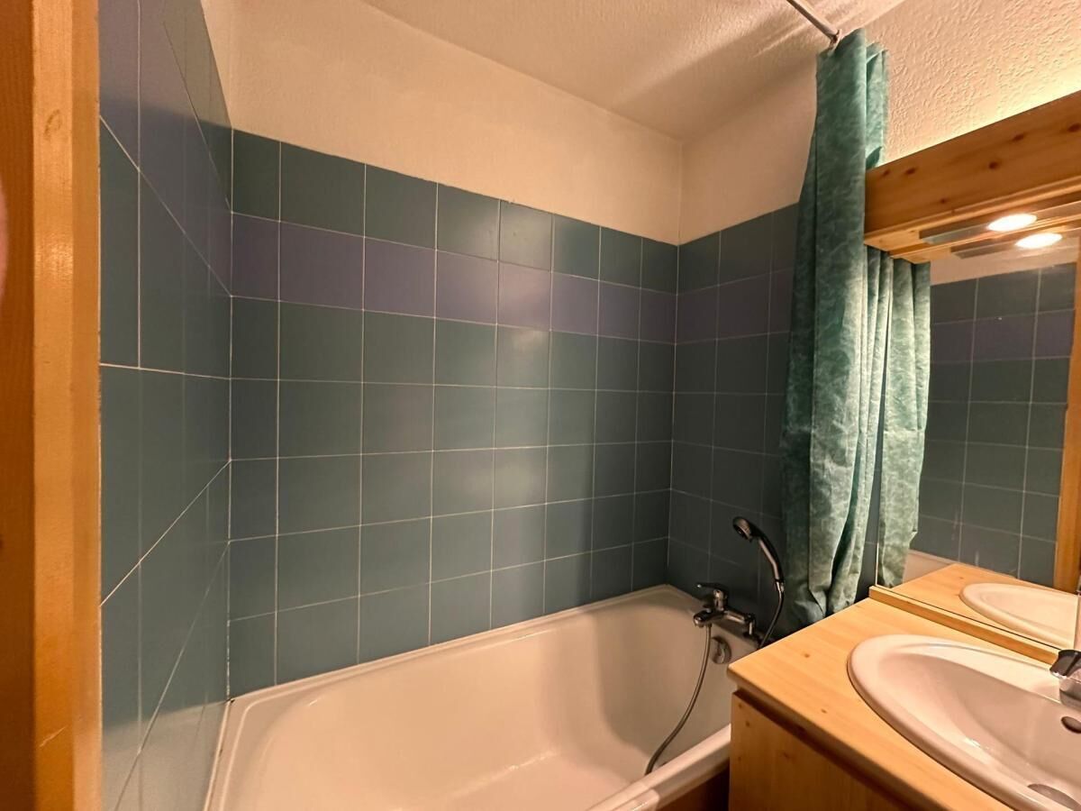 Une salle de bain avec une baignoire, un meuble-lavabo en bois avec un miroir et des carreaux de couleur turquoise sur les murs.