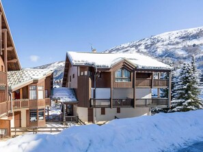 A multi-story wooden building with balconies and a snow-covered roof, surrounded by snow and mountains. - Resort center, 1st floor, terrace, balcony, ski locker, 30m², Valloire (Valloire)