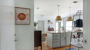 A modern kitchen with a central island, pendant lighting, and a coffee-themed wall art.