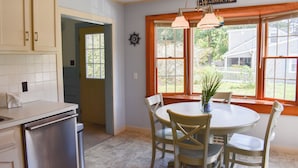 A kitchen with a dining area, featuring a white table, chairs, and a window with a view of the backyard. - Light and bright two bedroom home in Harwich featuring central air! (West Harwich)