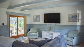 A living room with a grey sofa, two armchairs, a white cabinet, and a flat-screen TV mounted on the wall. - Light and bright two bedroom home in Harwich featuring central air! (West Harwich)