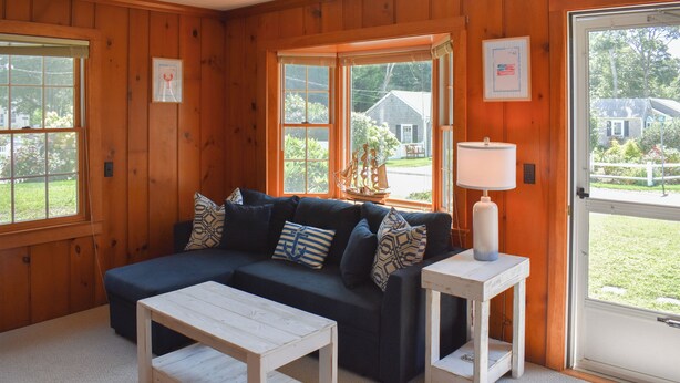 A cozy room with a dark blue sofa, patterned pillows, a wooden coffee table, and a side table with a lamp. - Light and bright two bedroom home in Harwich featuring central air! (West Harwich)