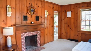 A room with wooden paneling, a fireplace, a table with a lamp, and a window. - Light and bright two bedroom home in Harwich featuring central air! (West Harwich)