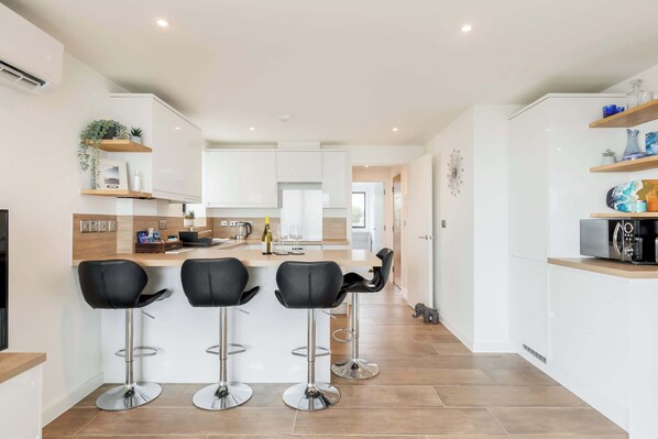 A modern kitchen with white cabinets, a central island with bar stools, and a microwave on the right.