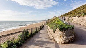 A coastal walkway with a stone wall, a beach, and the ocean. - Rise and Shine - With a Balcony On the Seafront (Christchurch)