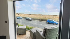 A balcony with wicker furniture overlooking a road and beach. - Rise and Shine - With a Balcony On the Seafront (Christchurch)