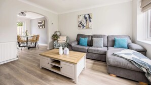 A modern living room with a grey sofa, a wooden coffee table, and a dining area with a table and chairs. - Shell Cove - With Sunny Rear Patio Near Harbourside Park (Poole)