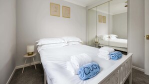 A hotel room with a neatly made bed, a bedside table with a lamp, a large mirror, and two framed pictures on the wall. - Shell Cove - With Sunny Rear Patio Near Harbourside Park (Poole)