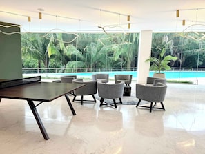 A modern indoor space with a pool view, a ping pong table, and grey upholstered chairs.