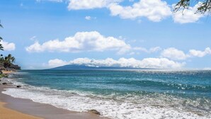 Une plage à l’eau d’un bleu limpide, bordée d’un rivage sablonneux, avec une montagne qui se profile à l’horizon.