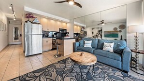 Une cuisine moderne dotée d’un îlot central, d’un coin repas avec un canapé bleu et une table basse, et d’un ventilateur de plafond.