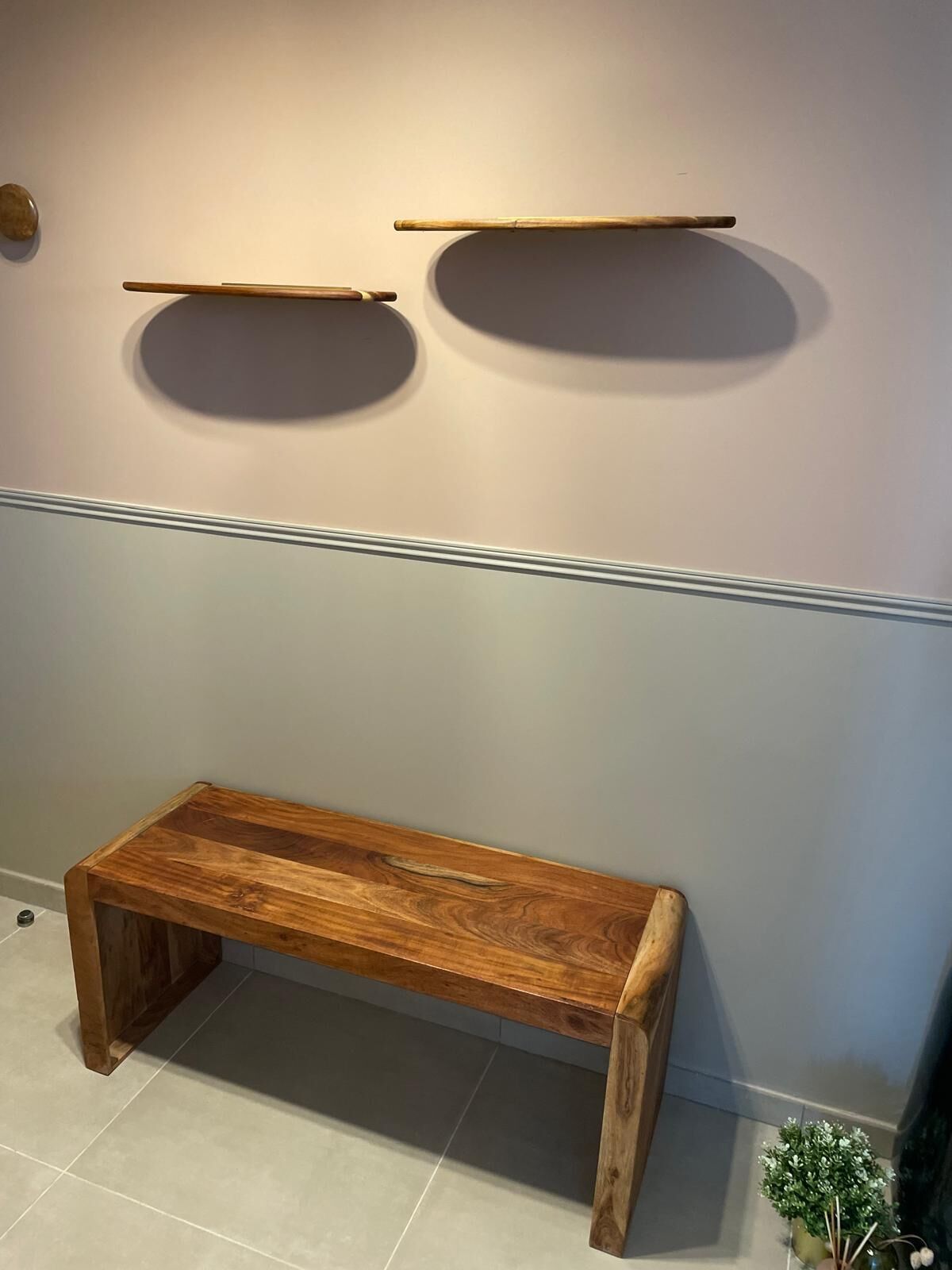 A wooden bench against a wall with two shelves above it.