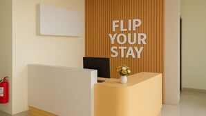 Un mostrador de recepción con un cartel que dice 'FLIP YOUR STAY', una computadora y un jarrón con flores.