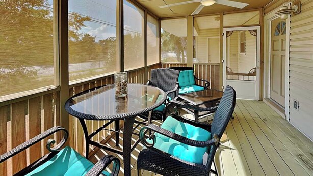 Une terrasse couverte avec une table en verre, des chaises en osier et un ventilateur de plafond.
