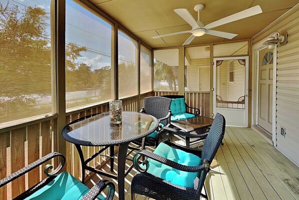 Une terrasse couverte avec une table en verre, des chaises en osier et un ventilateur de plafond.