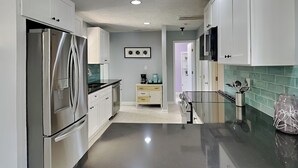 Une cuisine moderne dotée d’appareils électroménagers en acier inoxydable, d’un plan de travail noir et d’un pare-feu turquoise.