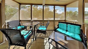 Une terrasse couverte, aménagée avec des meubles en osier, une table en verre et un ventilateur de plafond.