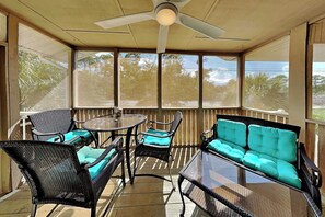 A covered patio with wicker furniture, a glass table, and a ceiling fan.