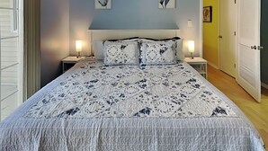 Une chambre à coucher comprenant un lit, deux tables de chevet, une commode, une porte et un mur orné de deux tableaux encadrés.