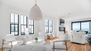 Amplia sala de estar con mobiliario blanco, ventanas grandes y vistas a la ciudad.