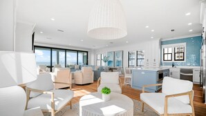 Un salón moderno con mobiliario blanco, una mesa de centro redonda y un amplio ventanal con vista a la ciudad.