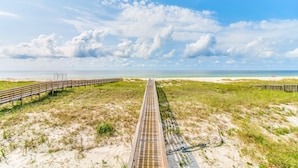 Un paseo marítimo que lleva a una playa con cielo despejado y nubes.