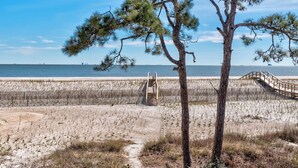 Une plage avec une promenade en bois menant à un escalier, une zone sablonneuse à la végétation clairsemée et une vue dégagée sur l’océan.