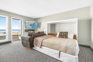 A hotel room with a bed, a television, a view of the beach, and a door leading outside. - Ocean view studio, no stairs-Full Kitchen, Patio! (Lincoln City)