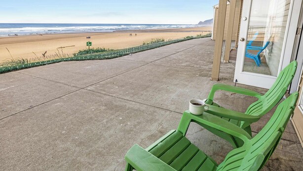 Uitzicht op het strand vanaf een overdekt terras, met een groene stoel en een witte beker erop.