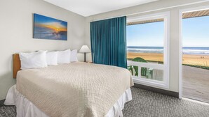 Een hotelkamer met een bed, een schilderij, een raam met uitzicht op het strand, en een gordijn.