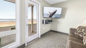Een kamer met een aan de muur bevestigde televisie, een deur naar een balkon met uitzicht op het strand, en een kamerbreed tapijt met een patroon.