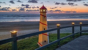 A lighthouse with a red top and yellow stripes, positioned next to a beach with a railing. - Oceanfront Ground Floor Studio  - Pool & Hot Tub! (Lincoln City)