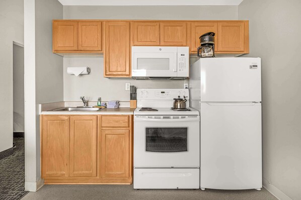 A compact kitchen with wooden cabinets, a white microwave, a stove, and a refrigerator.